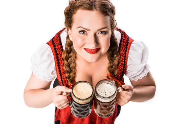 Високий кут зору на офіціантку в традиційній баварській сукні, що тримає кубки з легким і темним пивом ізольовано на білому тлі — стокове фото