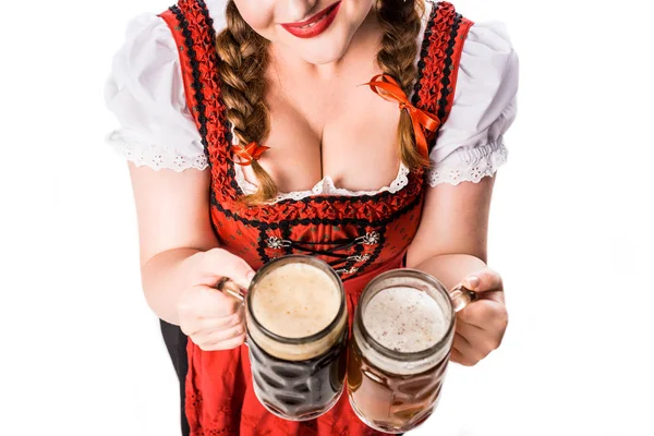 Imagen recortada de la camarera oktoberfest en vestido bavariano tradicional mostrando tazas con cerveza clara y oscura aislada sobre fondo blanco - foto de stock