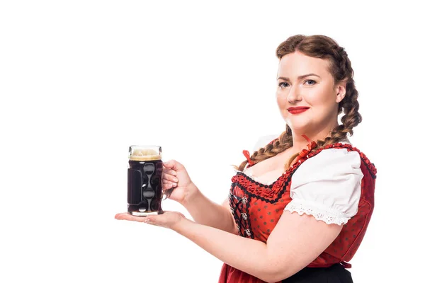 Feliz oktoberfest camarera en vestido bavariano tradicional sosteniendo taza de cerveza oscura aislada sobre fondo blanco - foto de stock