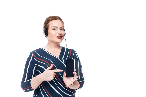 Operador femenino del centro de llamadas con auriculares apuntando al teléfono inteligente con pantalla en blanco aislada sobre fondo blanco - foto de stock