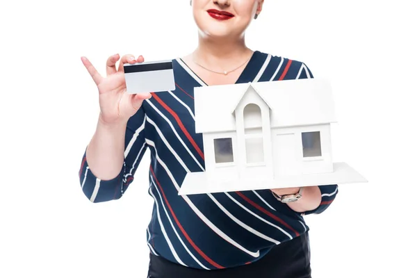 Imagen recortada de agente inmobiliario femenino mostrando maqueta de casa nueva y tarjeta de crédito aislada sobre fondo blanco - foto de stock