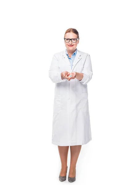 Sorridente médico feminino em óculos mostrando pílulas isoladas em fundo branco — Fotografia de Stock