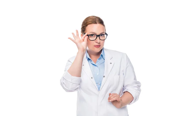 Attractive female doctor adjusting eyeglasses and looking at camera isolated on white background — Stock Photo