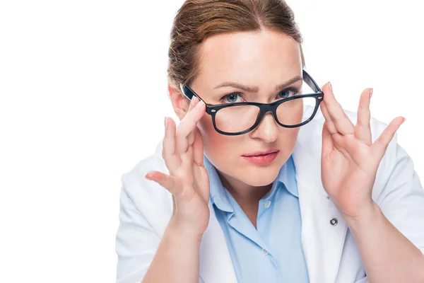 Grave médecin féminin ajuster les lunettes et regarder la caméra isolée sur fond blanc — Photo de stock