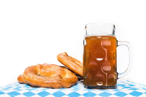 Primer plano vista de taza de cerveza y pretzels en mesa con mantel sobre fondo blanco - foto de stock