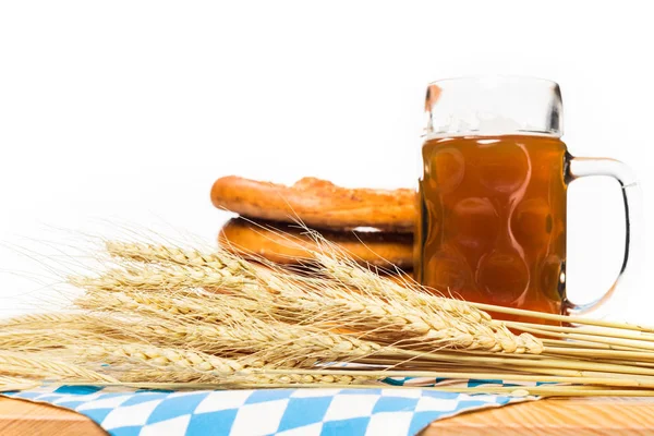 Vue rapprochée des épis de blé, tasse de bière et bretzels sur table avec nappe sur fond blanc — Photo de stock