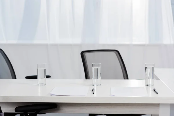 Primo piano di scrivania con bicchieri d'acqua e carte bianche in ufficio moderno — Foto stock