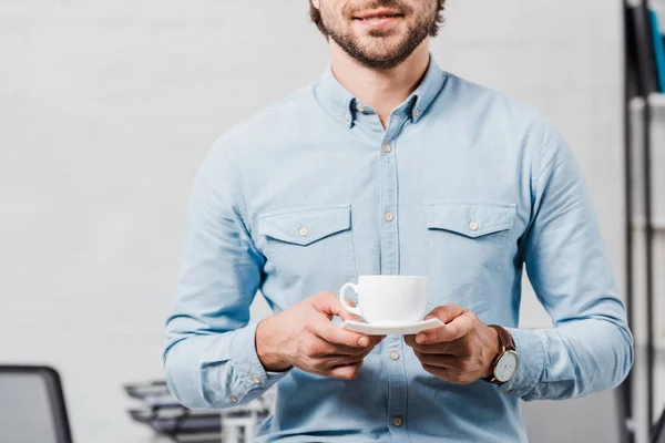 Tiro cortado de jovem empresário com xícara de café no escritório moderno — Fotografia de Stock