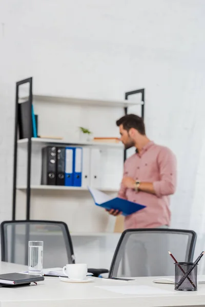 Nahaufnahme eines Tisches im Konferenzsaal mit einem jungen Geschäftsmann, der einen Ordner mit Dokumenten hält, die im Hintergrund verschwommen sind — Stockfoto