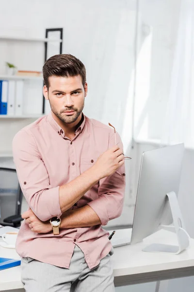 Handsome young businessman leaning back at workplace and looking at camera — Stock Photo