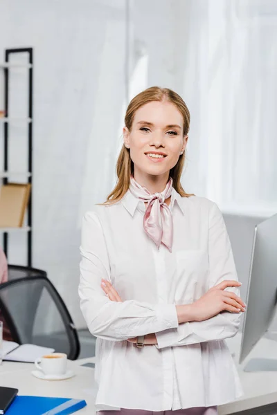 Beautiful young businesswoman with crossed arms looking at camera at modern office — Stock Photo