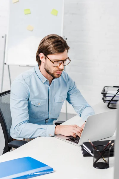 Giovane uomo d'affari concentrato che lavora con computer portatile in ufficio moderno — Foto stock