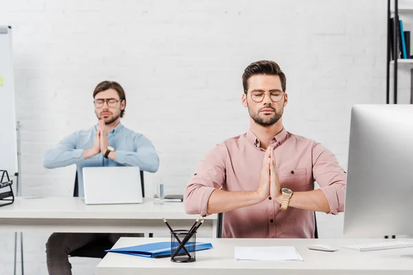 Guapos hombres de negocios meditando y haciendo namaste mudra en la oficina moderna - foto de stock