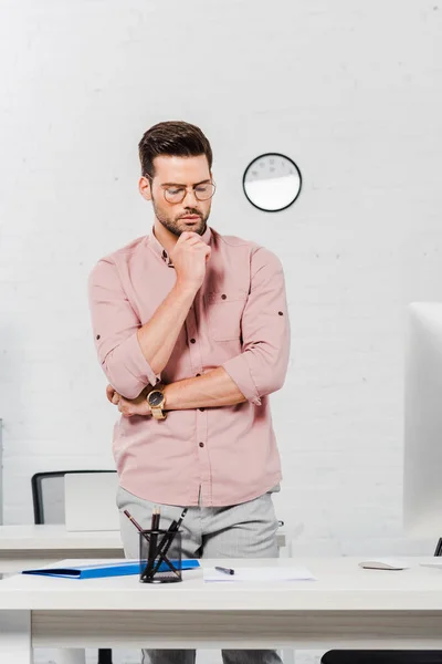 Réfléchi jeune homme d'affaires debout près du lieu de travail au bureau moderne — Photo de stock