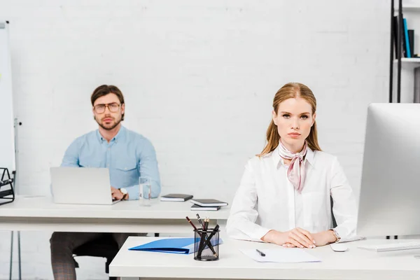 Seriöse Geschäftspartner sitzen am Arbeitsplatz im modernen Büro und schauen in die Kamera — Stockfoto