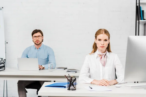 Seri colleghi di lavoro seduti nei luoghi di lavoro presso l'ufficio moderno e guardando la fotocamera — Foto stock