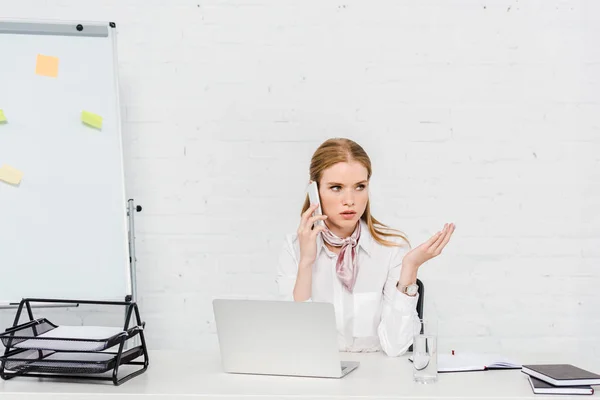 Emotional young businesswoman talking by phone at workplace — Stock Photo