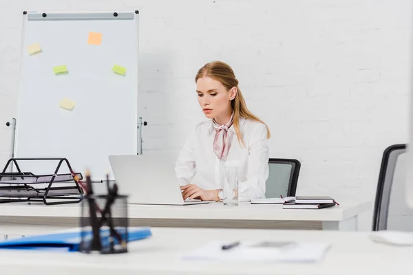 Selbstbewusste junge Geschäftsfrau arbeitet mit Laptop im modernen Büro — Stockfoto