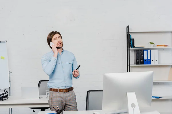 Emotional young businessman looking up while talking by phone at modern office — Stock Photo