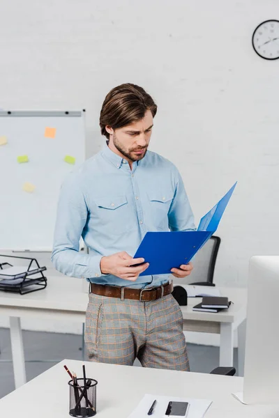 Beau jeune homme d'affaires lisant des documents dans le dossier au bureau moderne — Photo de stock