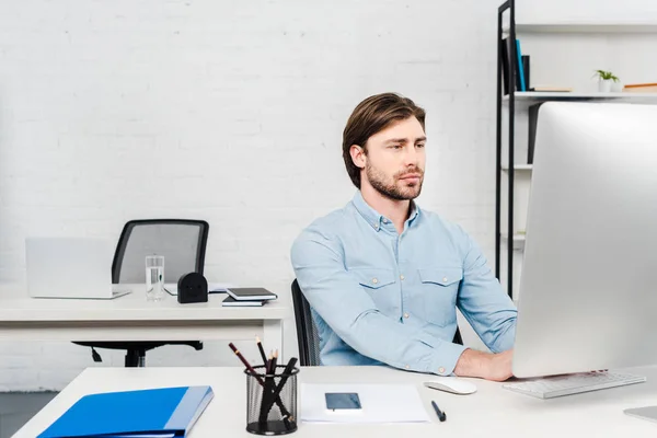 Schöner junger Geschäftsmann arbeitet mit Computer in modernem Büro — Stockfoto