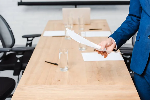 Обрезанный снимок бизнесмена, держащего пустую бумагу за столом для конференций в офисе — стоковое фото