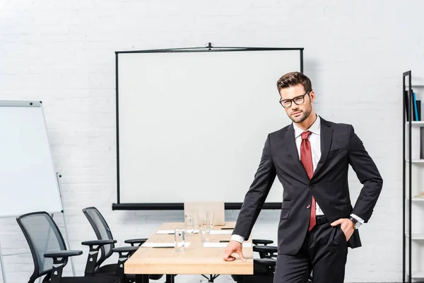 Joven hombre de negocios guapo mirando la cámara en la sala de conferencias con tablero de presentación en blanco - foto de stock