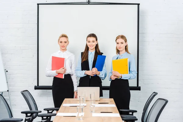 Successful young businesswomen with folders of documents looking at camera at conference hall — Stock Photo