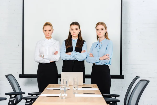 Attractive young businesswomen with crossed arms looking at camera at conference hall — Stock Photo