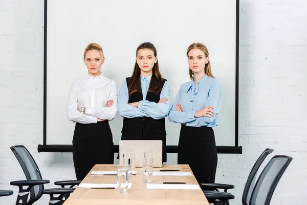 Atractivas jóvenes empresarias con brazos cruzados mirando a la cámara en la sala de conferencias - foto de stock