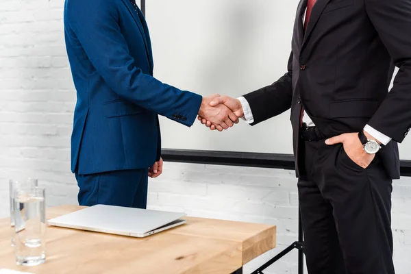 Recortado tiro de hombres de negocios estrechando la mano en la oficina moderna - foto de stock