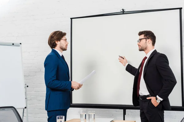Geschäftsleute unterhalten sich und zeigen auf Präsentationstafel in modernem Büro — Stockfoto