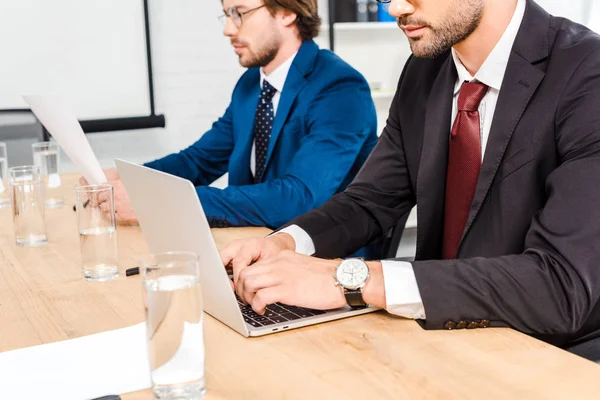 Обрізаний знімок бізнесменів, які працюють з документами та ноутбуком разом в сучасному офісі — стокове фото