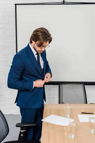 Attractive young businessman reading documents and buttoning jacket at modern office — Stock Photo