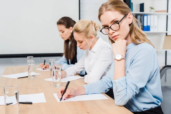 Selbstbewusste junge Geschäftsfrauen sitzen im Konferenzsaal und schreiben Dokumente — Stockfoto