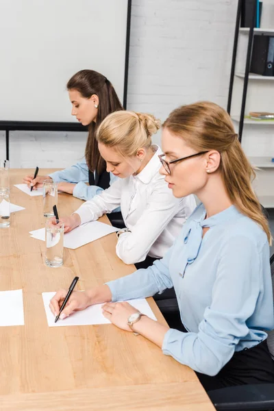 Focused young businesswomen sitting at conference hall and writing documents — Stock Photo