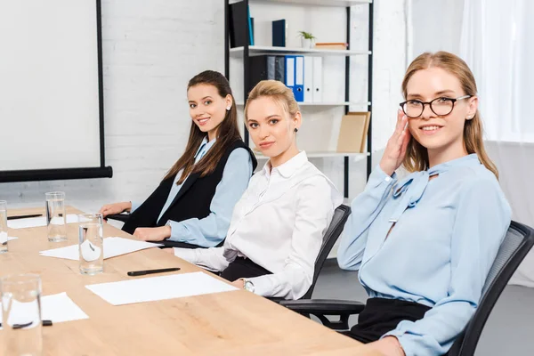 Confident young businesswomen sitting at conference hall and looking at camera — Stock Photo