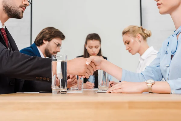 Recortado disparo de socios de negocios estrechando la mano durante la conferencia en la oficina moderna - foto de stock