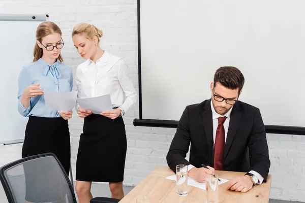 Junge Geschäftsfrauen diskutieren Papiere, während der Chef im modernen Büro Dokumente schreibt — Stockfoto