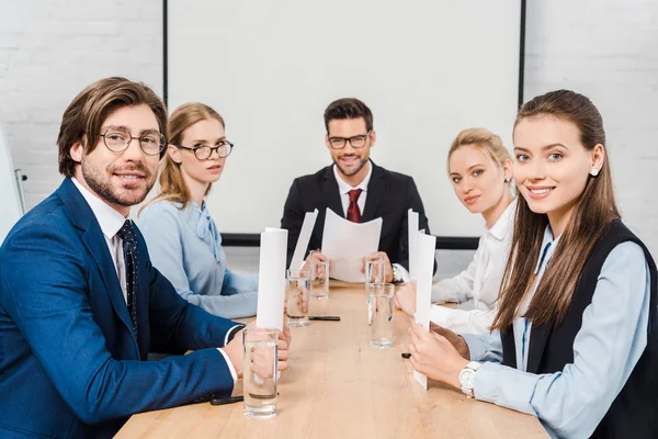 Команда улыбающихся деловых людей, сидящих в конференц-зале и смотрящих в камеру — стоковое фото