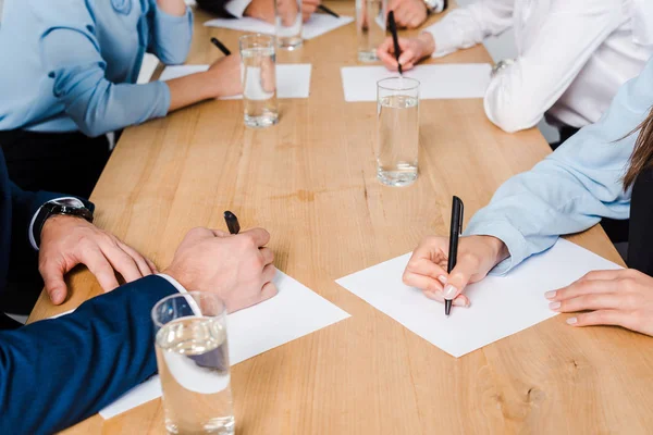 Tiro recortado de equipe de empresários escrevendo em papéis em branco na sala de conferências — Fotografia de Stock