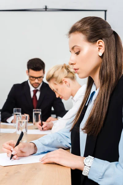 Attraktive junge Geschäftsfrau schreibt während einer Konferenz mit Kollegen auf leeres Papier — Stockfoto