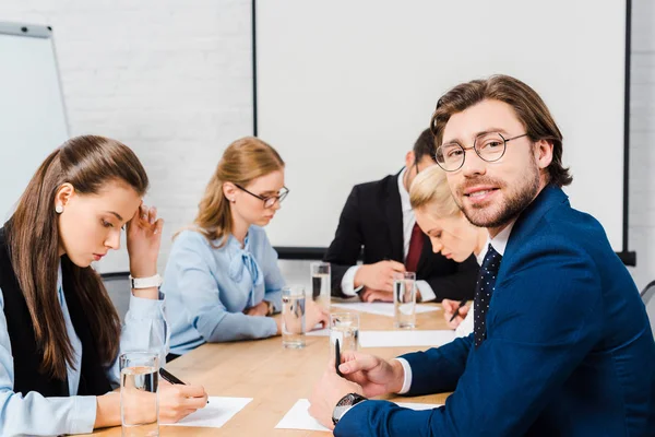 Sonriente joven hombre de negocios sentado en la sala de conferencias con colegas durante la conversación - foto de stock