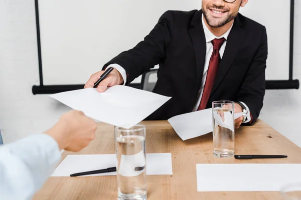 Cropped shot of businessman passing blank papers to female colleague at office — Stock Photo