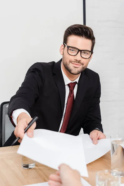 Tiro recortado de homem de negócios sorrindo passando papéis em branco para colega no escritório — Fotografia de Stock