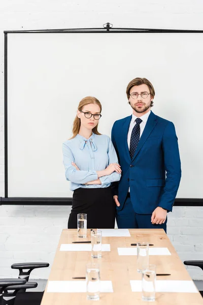 Business people standing at modern office and looking at camera in front of blank presentation board — Stock Photo