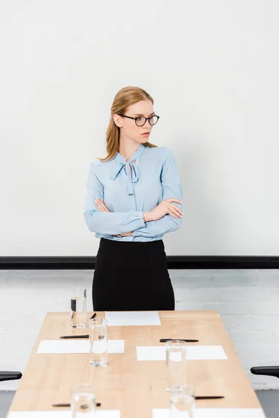 Serious young businesswoman with eyeglasses at conference hall looking away — Stock Photo