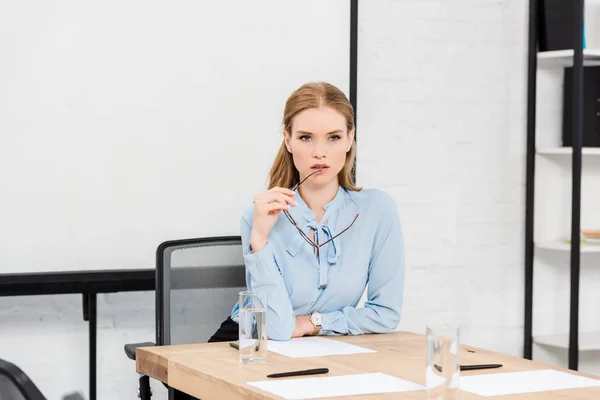 Réfléchie jeune femme d'affaires avec des lunettes au bureau moderne regardant la caméra — Photo de stock