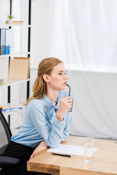 Nachdenkliche junge Geschäftsfrau mit Brille im modernen Büro, die wegschaut — Stockfoto