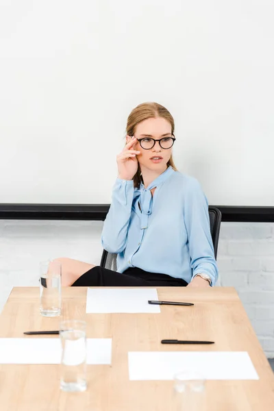 Schöne junge Geschäftsfrau sitzt allein im Konferenzsaal und schaut weg — Stockfoto